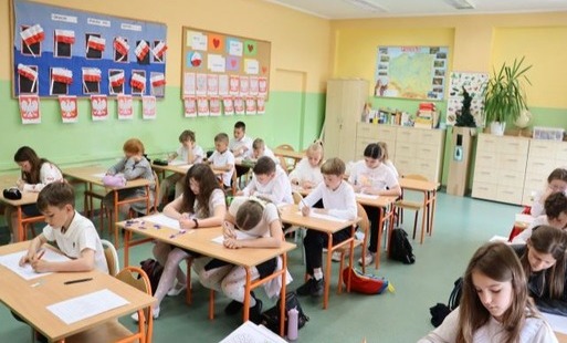Zdjęcie klasy i uczniów siedzących w ławkach i piszących egzamin trzeciklasisty